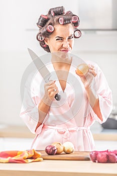 Female with hair rollers and silk pyjamas frowns upon the need to cut the onion by a knife