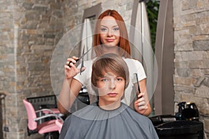 Female hairdresser cutting hair of man client and looking into camera.