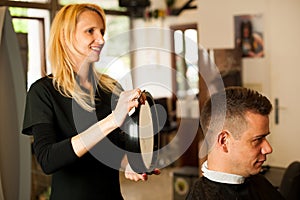 Female hairdresser cutting hair of smiling man client at beauty