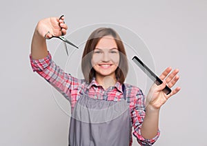 Female hairdresser holding scissors and comb at gray background