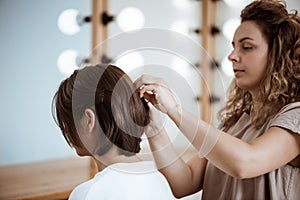 Female hairdresser making hairstyle to brunette girl in beauty salon.