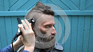 Female hairdresser making male haircut with hair clipper in hairdressing salon on open air