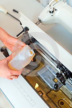 Female hand adding oil in sewing machine.