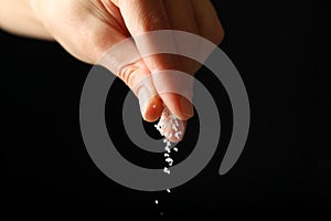 Female hand adding salt on black background photo