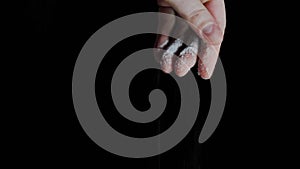 Female hand adding white salt to dish against black background