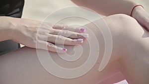 Female hand applying sun spray on her legs suntanning on the beach close-up. Summertime leisure. Body care