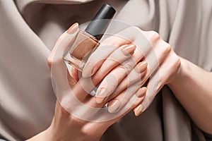Female hand with beige nail design. Brown nail polish manicure. Woman hand hold beige nail polish bottle
