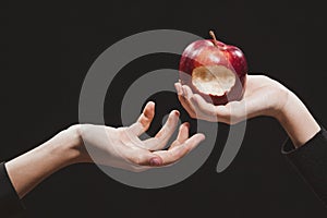 Female hand with a bitten red apple stretching it into a man`s hand