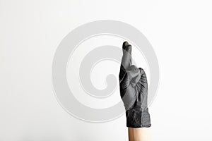 Female hand in black latex gloves crossing fingers for hope, on white background with free space for text