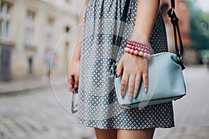 Female hand with blue handbag. Female hand with manicure and bracelets holding sunglasses. Stylish woman in dress with accessories