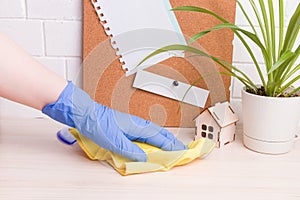 a female hand in a blue rubber glove wipes a desktop with a yellow rag