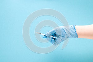 female hand in a blue rubber medical glove holds an insulin syringe on a blue background copy space, treatment and health care con