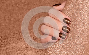 Female hand with brown nail design. Glitter brown nail polish manicure. Woman hand on glitter beige fabric background