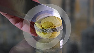 female hand carelessly crumbles and cuts macarons with french dessert with a knife on a glass table close-up yellow