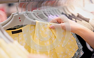 Female hand choosing clothes for checked pattern cotton dress on the rack in cloth shop at department store