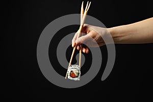 Female hand with chopsticks hold sushi roll on background. Japanese food