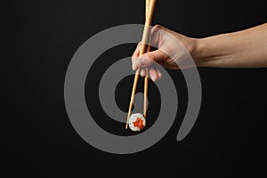 Female hand with chopsticks hold sushi roll on background. Japanese food