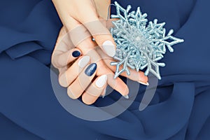 Female hand with Christmas nail design. Glitter blue and matte white nail polish manicure. Model hand hold blue Christmas star on