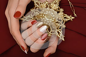 Female hand with Christmas nail design. Red and gold nail polish manicure. Female hand hold golden New Year star