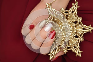 Female hand with Christmas nail design. Red and gold nail polish manicure. Female hand hold golden New Year star