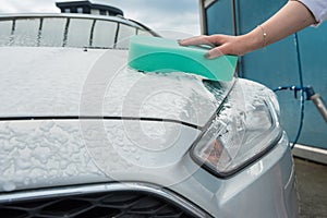 Female hand cleaning car in service with tools soap foam and water