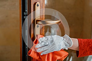 Female hand Cleaning front door handle by antibacterial alcohol detergent. Houseworker in white gloves clean Door knob by cloth