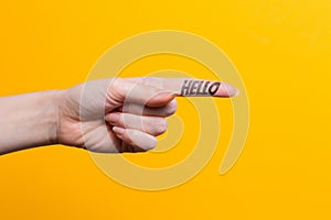 Female hand close-up, index finger pointing at something with text Hello. Gesture of direction. Yellow background. Copy space
