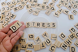 female hand closeup holds wooden alphabet blocks on background, changes word stress to distress, concept transient negative