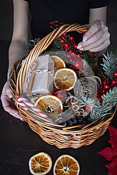 Female hand collects a wicker basket with Christmas decorations and goods as a gift