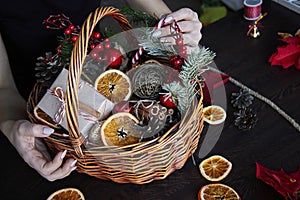 Female hand collects a wicker basket with Christmas decorations and goods as a gift