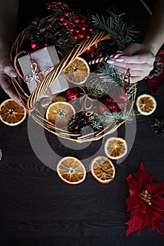 Female hand collects a wicker basket with Christmas decorations and goods as a gift