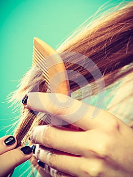 Female hand combing hair with wooden comb