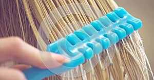 Female hand combing wet blond hair with a blue comb, close-up