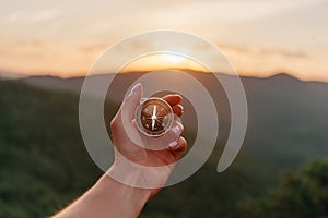 Female hand with compass in mountains at sunrise, pov.