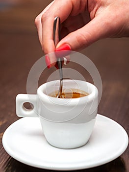 Female hand with cup of espresso coffee and spoon.