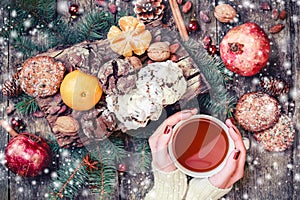 Female hand a cup of tea. Christmas Cookies Chocolate, tea, pomegranate, Tangerines, Nuts, cocoa beans on wooden snowy background.