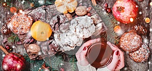 Female hand a cup of tea. Christmas Cookies Chocolate, tea, pomegranate, Tangerines, Nuts, cocoa beans on wooden snowy background.