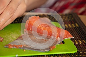 Female hand cut salmon into salad on a green board in the kitchen at the table