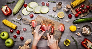 Female hand cut tomatoes on rustic grey background, around lie variety ingredients, vegetables, fruits, and spices, vegetarian foo