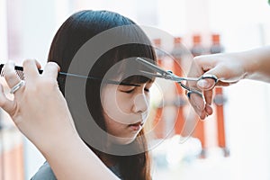 Female hand cuts hair for Asian girl with scissors and comb.