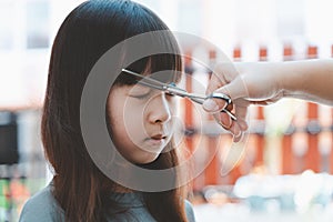 Female hand cuts hair for Asian girl with scissors and comb.