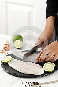 Female Hand Cutting Dori Fillet above Stone Board