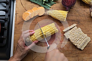 Female hand cutting fresh corn cob in half on a wooden cutting board