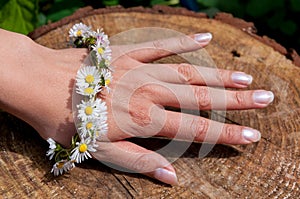 Female hand with daisy flower bracelet in the sun with a wooden