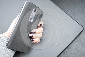 Female hand with dark nails holds a mobile phone with a knitted nylon back, which lies on a closed textured laptop cover