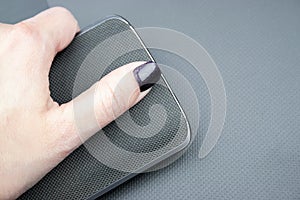 Female hand with dark nails holds a mobile phone with a knitted nylon back, which lies on a closed textured laptop cover