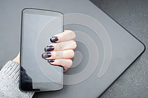 Female hand with dark nails holds a mobile phone, which lies on a closed laptop