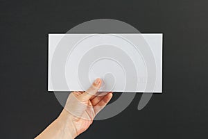 Female hand delivering a white envelope on black background