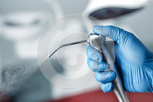 Female hand of dentist in blue gloves holding air water syringe, blurred background of clinic with dental unit, dentistry and photo