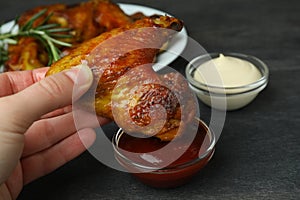 Female hand dipping baked chicken wing into sauce, close up